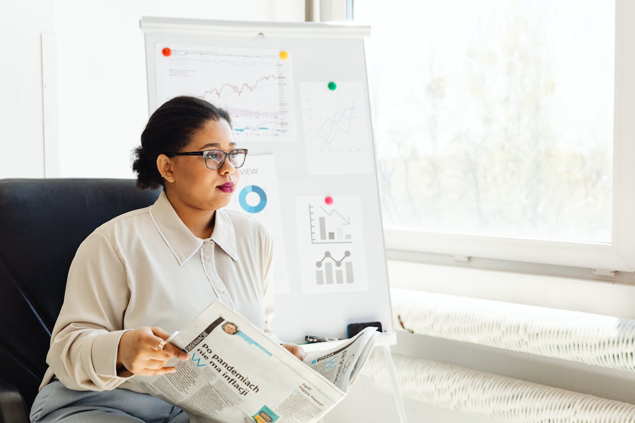 Confident businesswoman reading newspaper and analyzing market trends in a modern office setting.